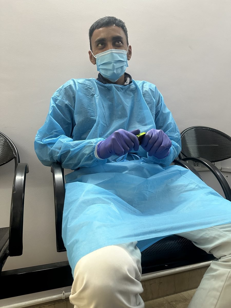 Ocularist in gown and gloves seated with a draped patient during a fitting